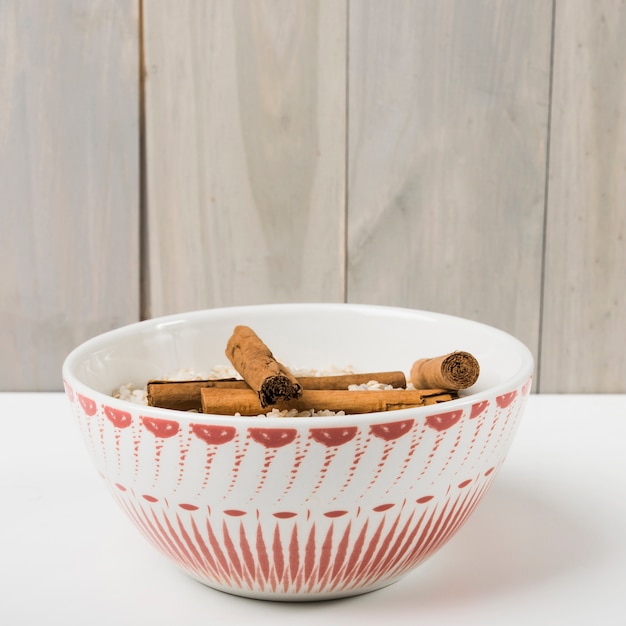 Foto gratuita palitos de canela con el tazón de arroz crudo en la mesa sobre fondo de madera