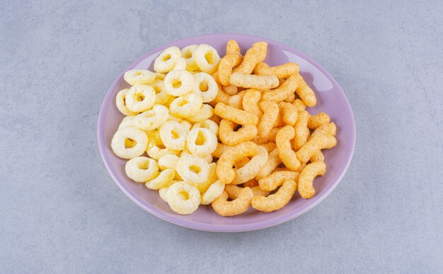 Palitos de maíz y anillos de maíz en un plato, sobre el mármol.