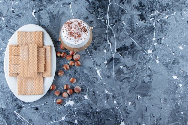 Palitos de oblea con nueces de macadamia y una taza de cristal de sabroso café caliente.