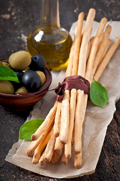 Palitos de pan grissini con jamón, aceitunas, albahaca sobre madera vieja