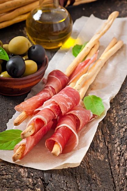 Foto gratuita palitos de pan grissini con jamón, aceitunas, albahaca sobre madera vieja