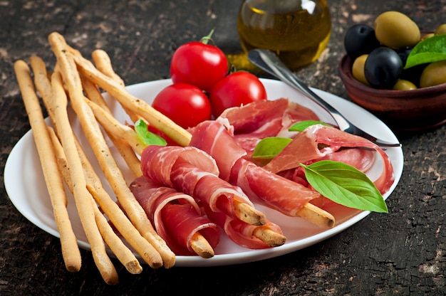 Foto gratuita palitos de pan grissini con jamón, aceitunas, albahaca sobre madera vieja