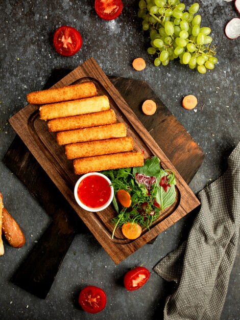 Palitos de queso rebozados sobre una plancha de madera