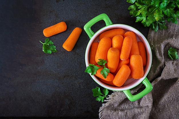 Palitos de zanahoria bebé en un tazón verde sobre una superficie negra. Concepto de alimentación saludable Comida vegana. Vista superior. Lay Flat