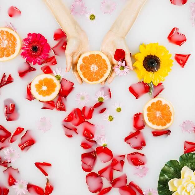 La palma de la mujer con pomelo, pétalos y flores en aguas claras