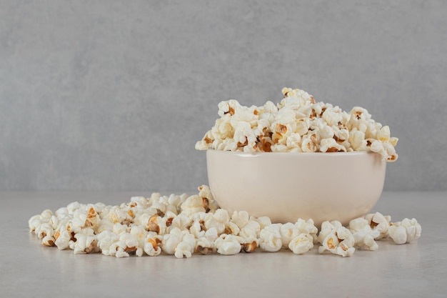 Palomitas de maíz crujientes dentro y alrededor de un recipiente blanco sobre superficie de mármol.