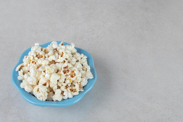 Palomitas de maíz crujientes en una pequeña bandeja azul sobre mesa de mármol.