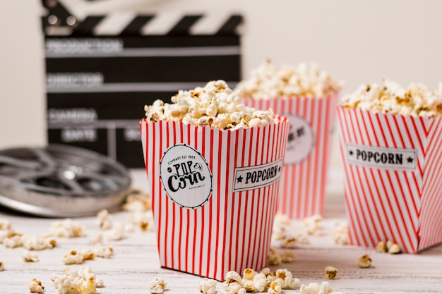 Palomitas de maíz en el cubo de tres bandas con rollo de película y claqueta sobre tabla de madera