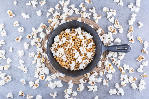 Palomitas de maíz esparcidas alrededor de una sartén con granos de maíz en la superficie de mármol