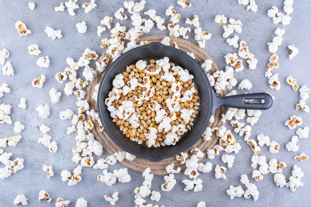 Palomitas de maíz esparcidas alrededor de una sartén con granos de maíz en la superficie de mármol