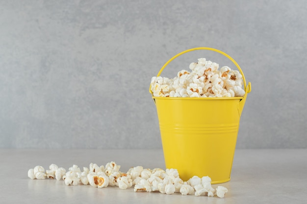 Foto gratuita palomitas de maíz metidas en un balde pequeño y esparcidas sobre mármol.