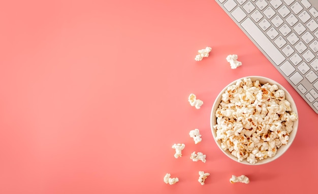 Palomitas de maíz y teclado sobre fondo rosa plano