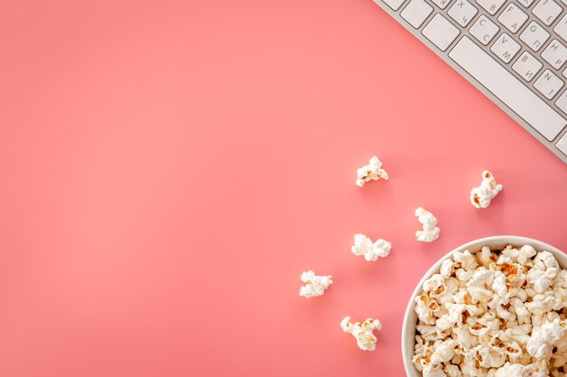 Palomitas de maíz y teclado sobre fondo rosa plano