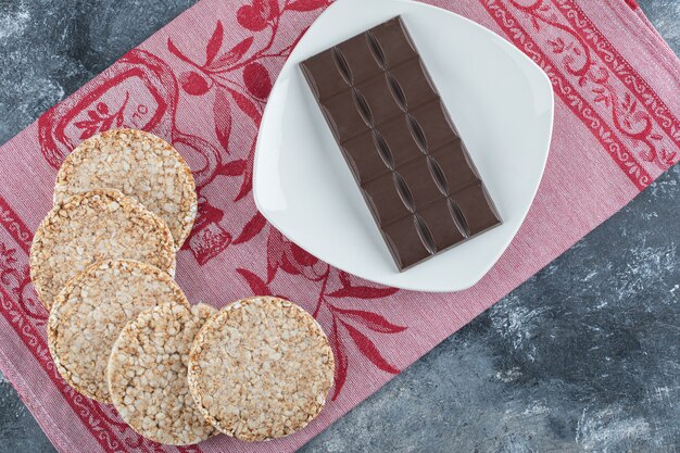 Pan de arroz crujiente con barra de chocolate sobre un mantel.