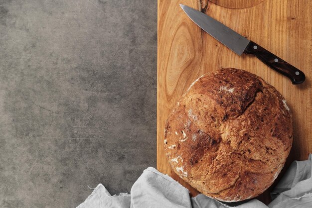 Foto gratuita pan casero de pan de masa madre artesanal en una tabla de cortar junto a un cuchillo sobre un fondo de hormigón gris vista de reconciliación con espacio para texto