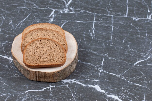 Pan de centeno en rodajas sobre plancha de madera sobre gris.