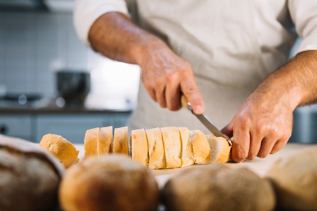 Pan de corte masculino con cuchillo en el mostrador de la cocina