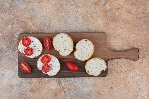 Pan con crema y rodajas de tomate sobre tabla de madera