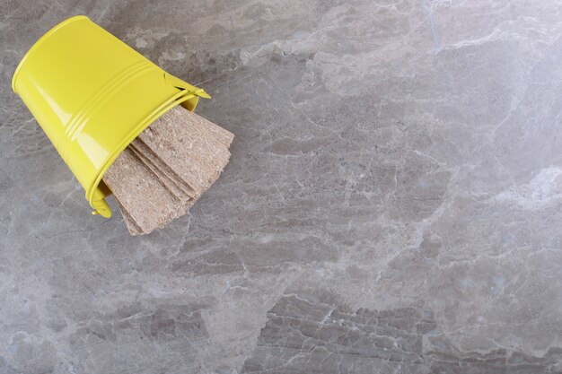 Pan crujiente cayendo del cubo amarillo volcado, sobre la superficie de mármol