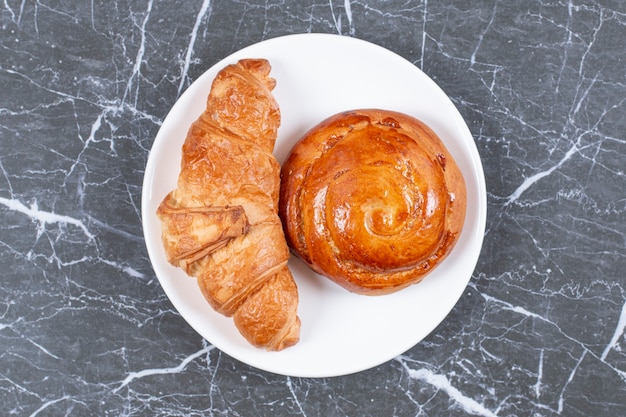 Pan dulce casero y croissant en el plato, sobre la superficie de mármol