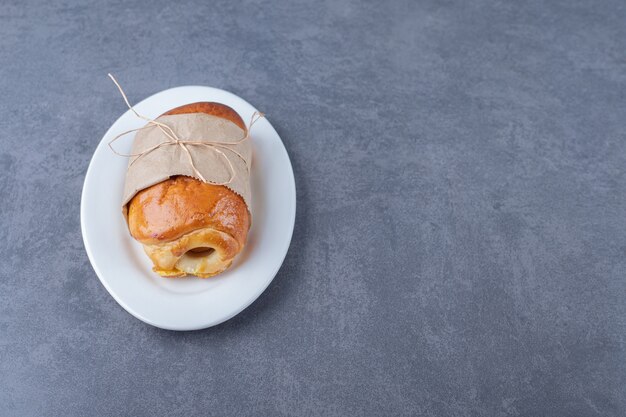 Pan dulce envuelto en papel en un plato, sobre el mármol.