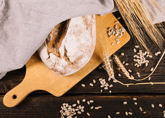 Pan y espiga de trigo con semillas de girasol en mesa de madera oscura