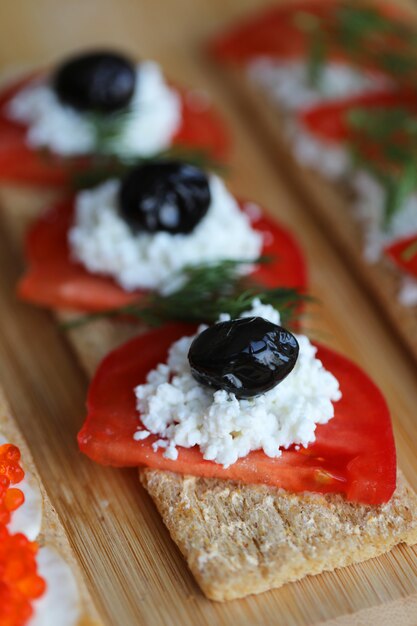 Pan de galleta con tomate, aceitunas negras y queso blanco.