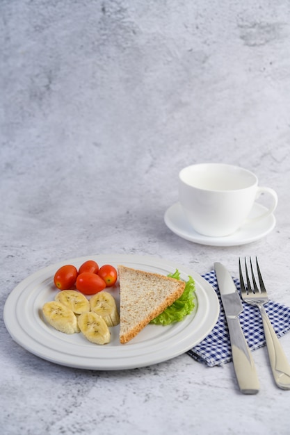 Foto gratuita pan, plátano y tomate en un plato blanco con tenedor y cuchillo.