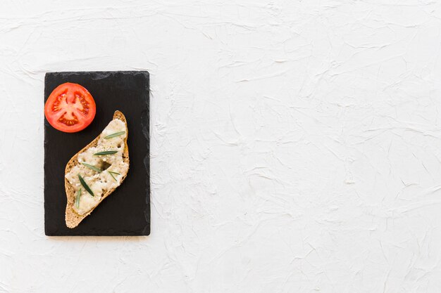 Pan de queso con rodaja de tomate en placa de pizarra sobre el fondo blanco