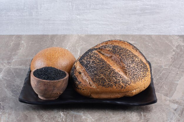 pan recubierto de sésamo negro y un tazón pequeño de semillas de sésamo negro en un plato sobre fondo de mármol. Foto de alta calidad