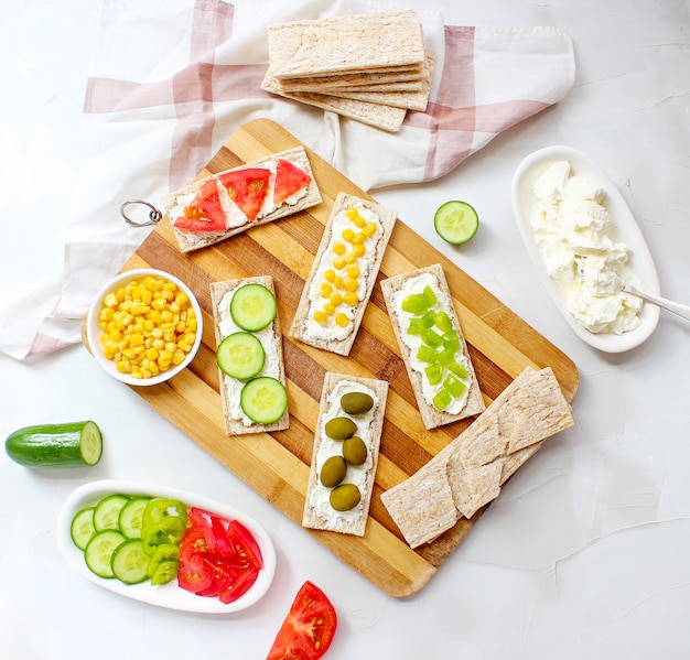 Pan tostado casero con queso cottage y aceitunas verdes, rodajas de col, tomate, maíz, pimiento verde en la tabla de cortar. Concepto de comida sana, vista superior. Lay Flat