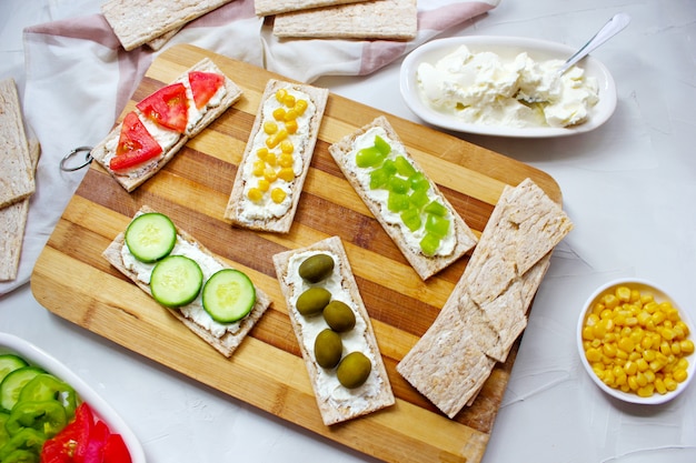 Pan tostado casero con queso cottage y aceitunas verdes, rodajas de col, tomate, maíz, pimiento verde en la tabla de cortar. Concepto de comida sana, vista superior. Lay Flat