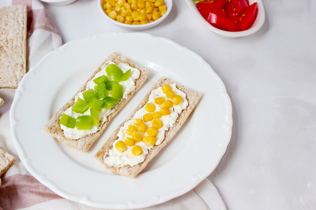 Pan tostado casero con queso cottage y aceitunas verdes, rodajas de col, tomate, maíz, pimiento verde en la tabla de cortar. Concepto de comida sana, vista superior. Lay Flat