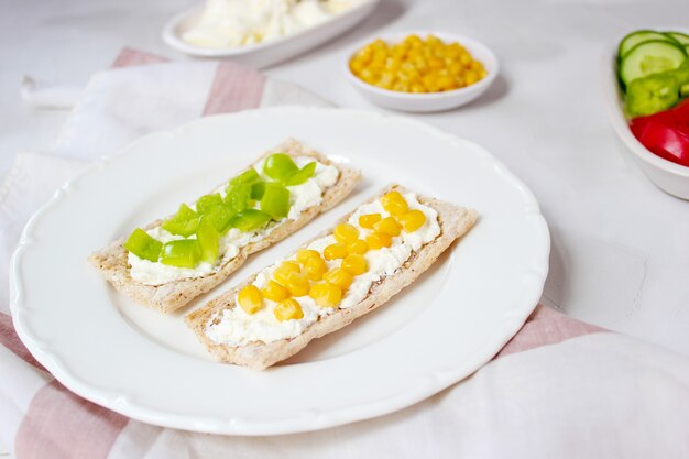 Pan tostado casero con queso cottage y aceitunas verdes, rodajas de col, tomate, maíz, pimiento verde en la tabla de cortar. Concepto de comida sana, vista superior. Lay Flat