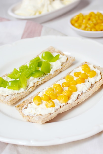 Pan tostado casero con queso cottage y aceitunas verdes, rodajas de col, tomate, maíz, pimiento verde en la tabla de cortar. Concepto de comida sana, vista superior. Lay Flat