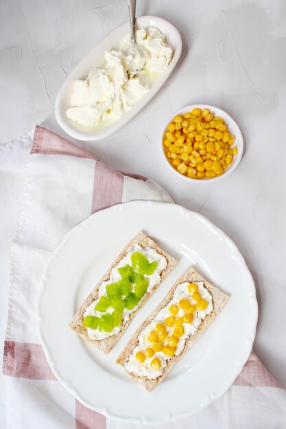 Pan tostado casero con queso cottage y aceitunas verdes, rodajas de col, tomate, maíz, pimiento verde en la tabla de cortar. Concepto de comida sana, vista superior. Lay Flat