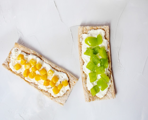 Pan tostado casero con queso cottage y aceitunas verdes, rodajas de col, tomate, maíz, pimiento verde en la tabla de cortar. Concepto de comida sana, vista superior. Lay Flat