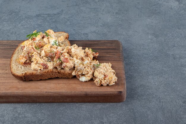 Pan tostado con ensalada de huevo sobre tabla de madera.