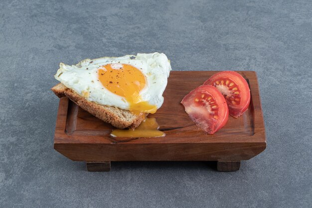 Pan tostado con huevo frito y tomates sobre tabla de madera