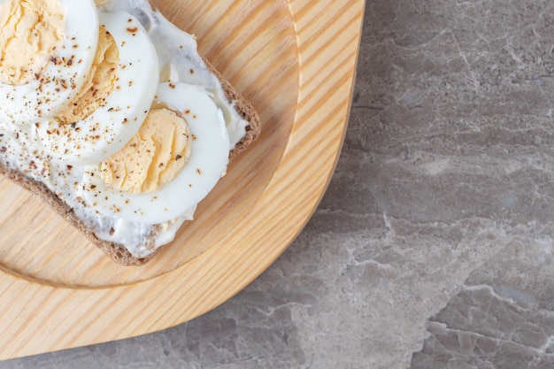 Pan tostado con huevos duros en placa de madera.