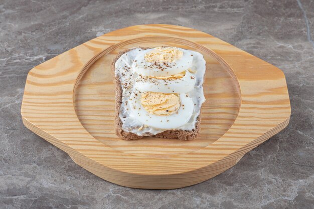 Pan tostado con huevos duros en placa de madera.