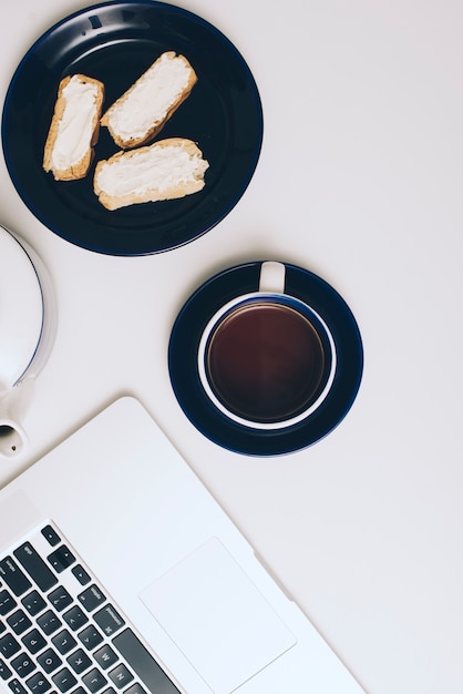 Pan tostado con queso crema; Taza de café y portátil sobre fondo blanco