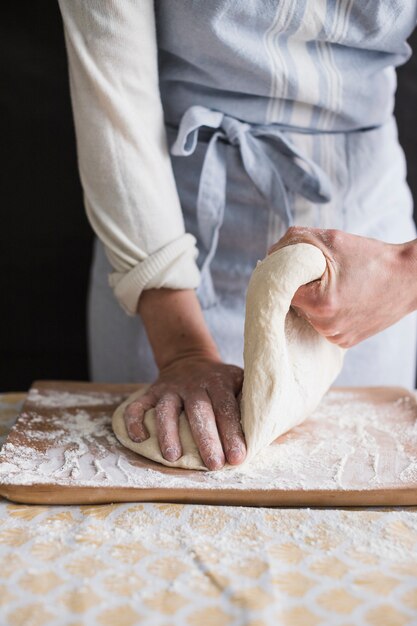 Una panadera que amasa la masa con harina en una tabla de cortar.