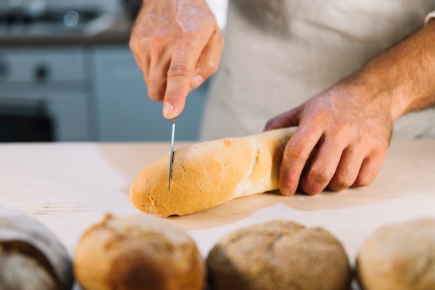 Panadero cortando pan con cuchillo en el mostrador de la cocina.