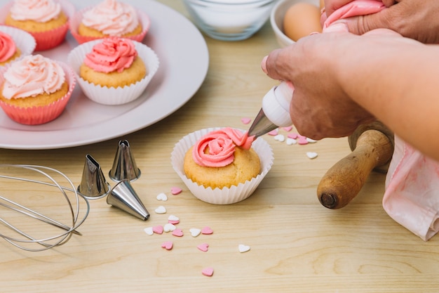 Panadero decora muffins con crema sobre el escritorio de madera