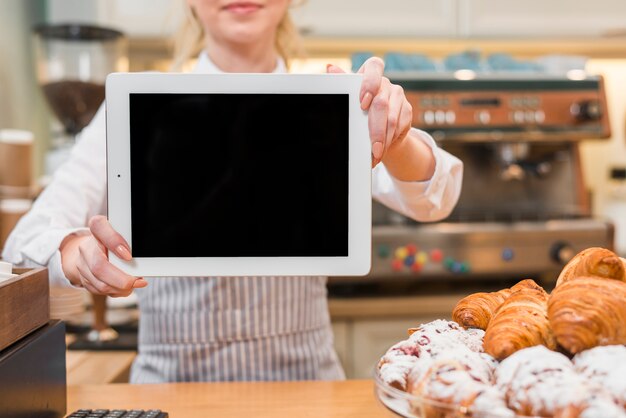 Panadero femenino mostrando tableta digital frente a croissant horneado en el mostrador