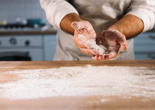 Foto gratuita panadero macho espolvoreado en mesa de madera con harina de trigo