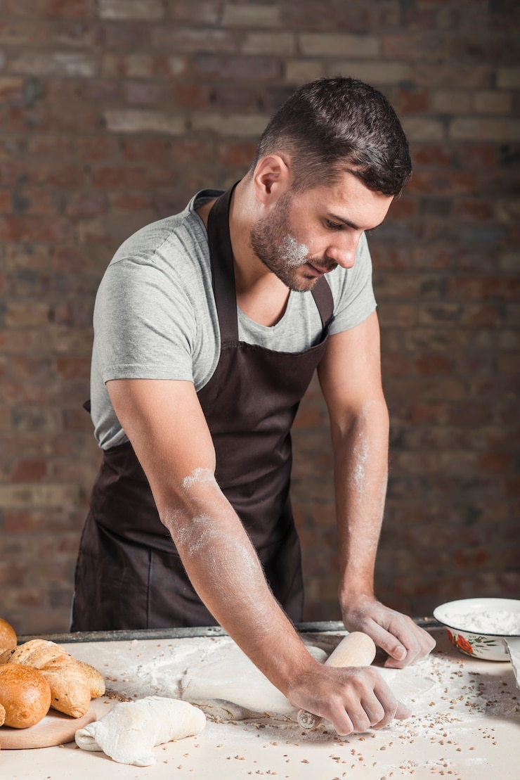 Foto gratuito panadero masculino rodando la masa con los pernos de balanceo en el mostrador de la cocina