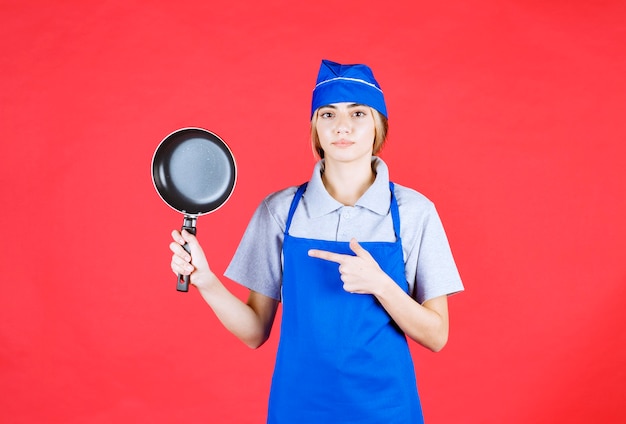 Foto gratuita panadero mujer en delantal azul sosteniendo una sartén tefal