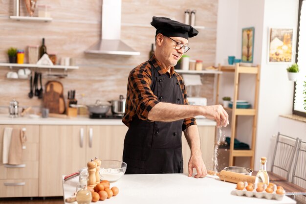 Foto gratuita panadero senior jubilado vistiendo delantal y bonete con ingredientes para pizza casera